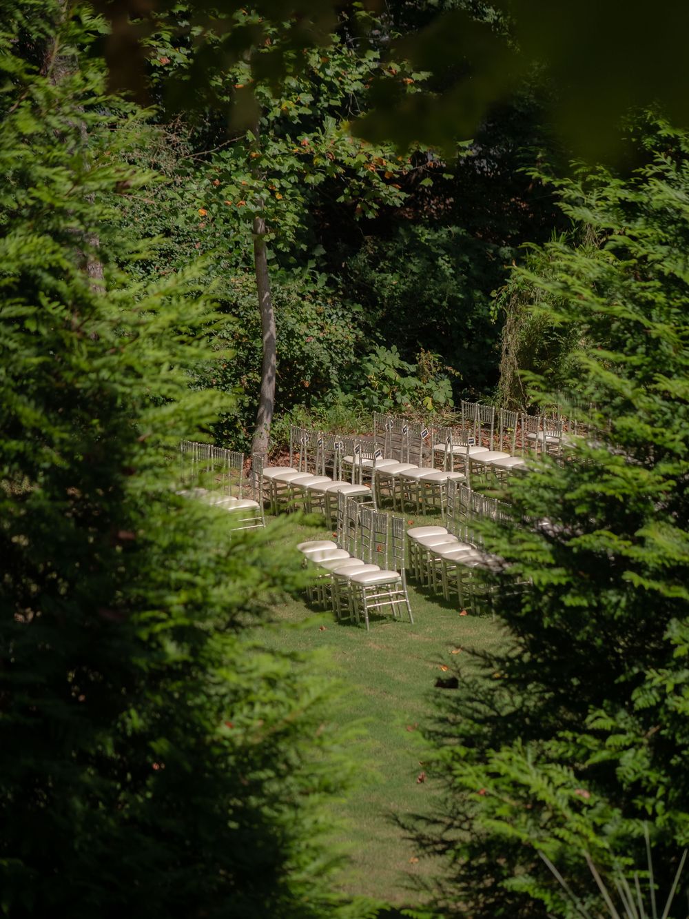 Aerial view of wedding ceremony seating arranged on a secluded lawn surrounded by trees.