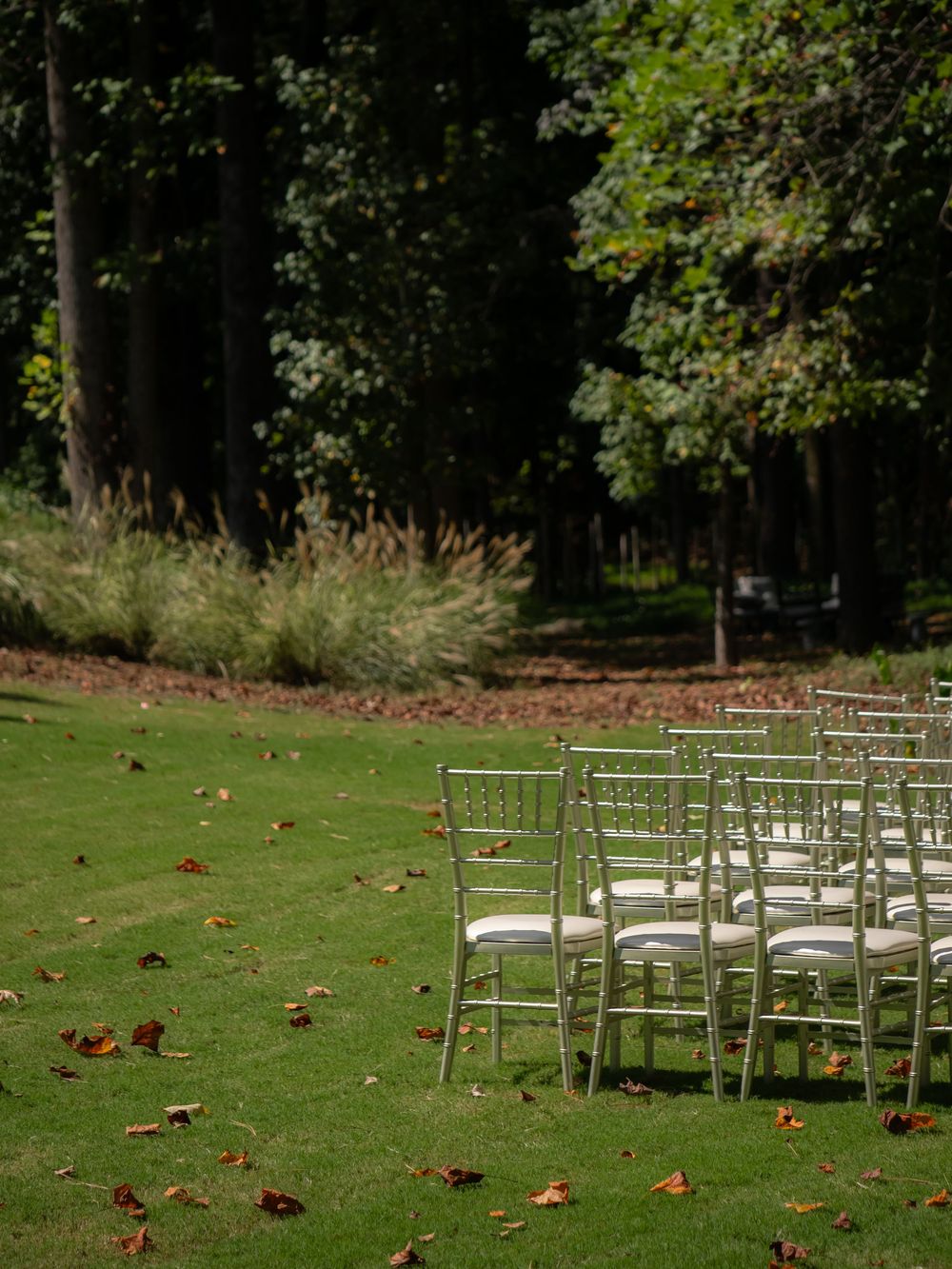 White chairs arranged in rows on a green lawn for an outdoor wedding ceremony.