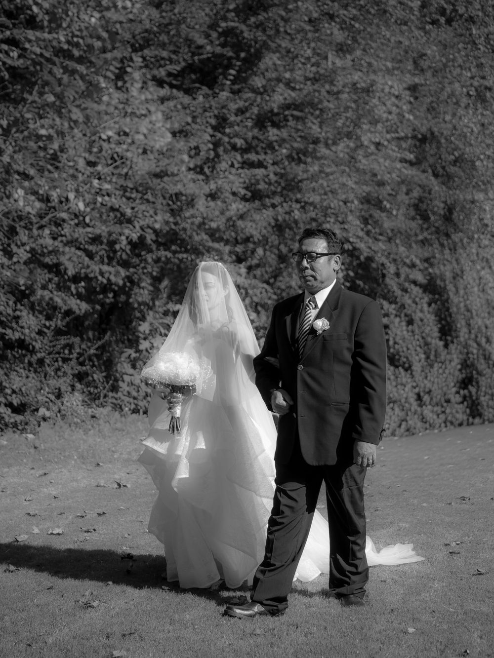 Black and white portrait of a bride and companion standing outdoors against a natural backdrop.