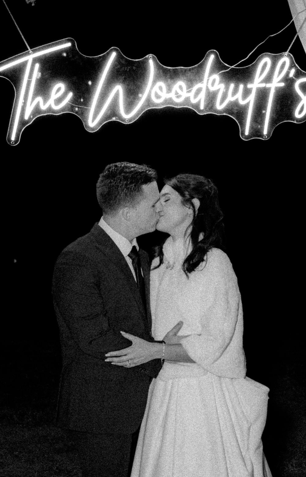 Intimate black and white photo under glowing neon signage at a wedding reception.