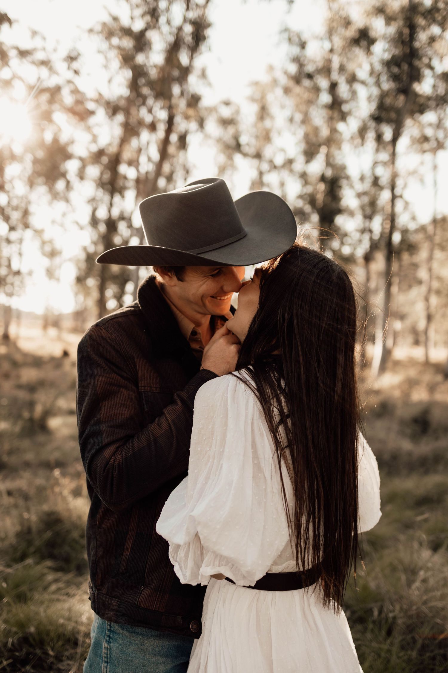 Couple embracing on a hilltop overlooking a vast landscape during sunset.