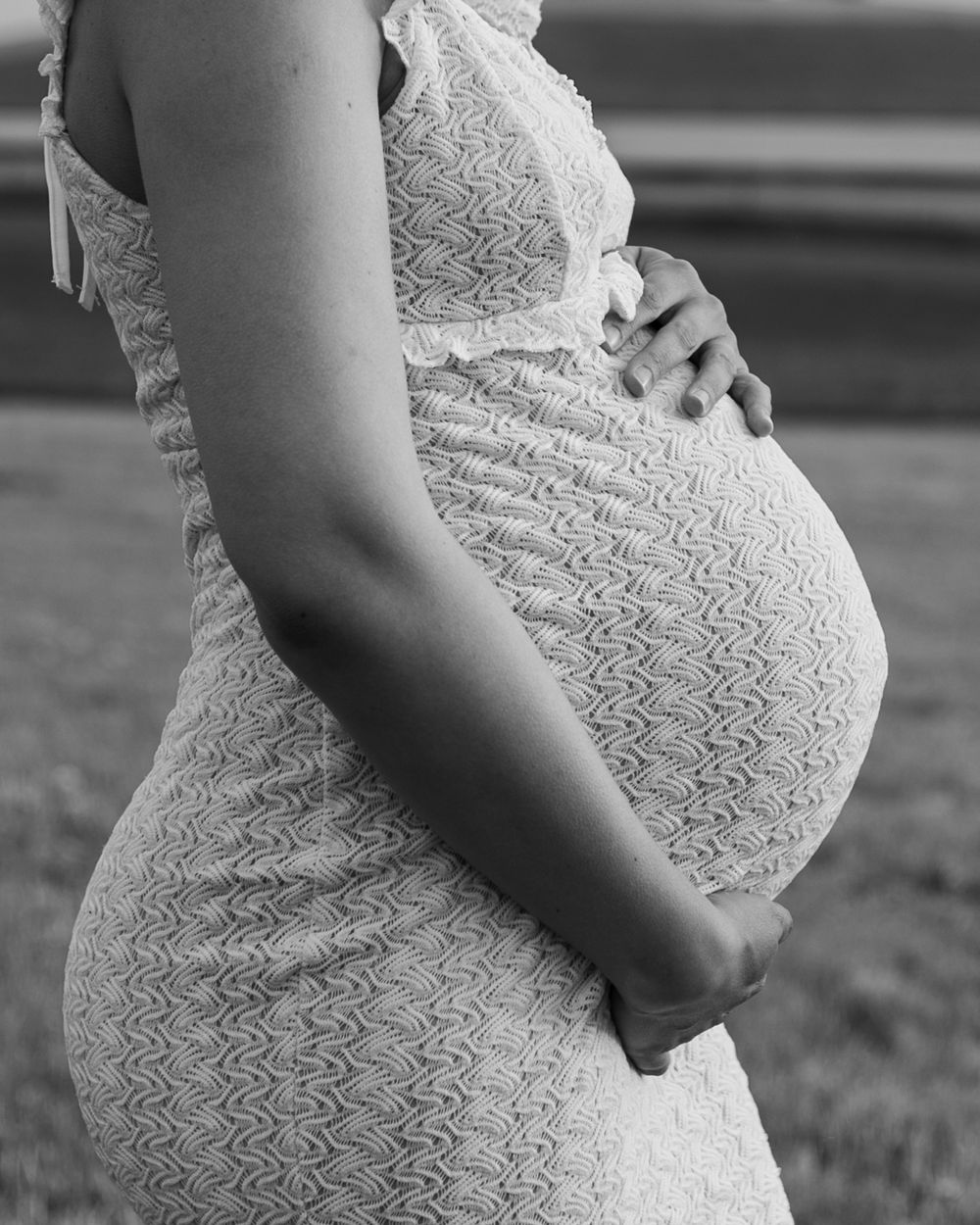 Close-up of pregnant belly in white lace maternity dress.