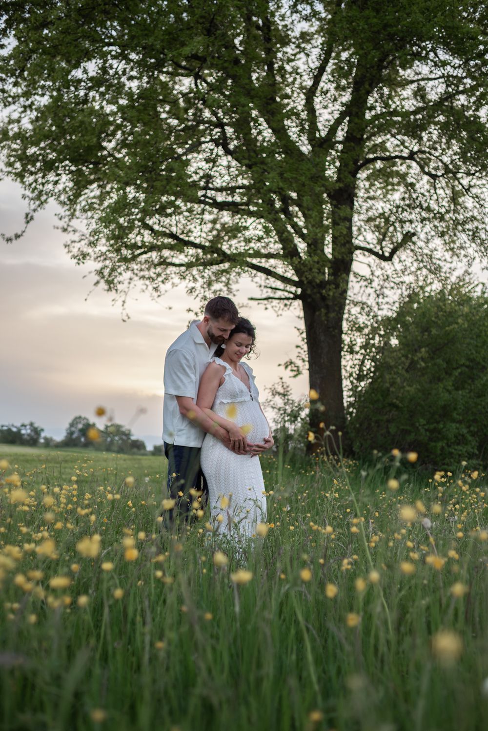 Couple standing together in field of yellow wildflowers during golden hour.