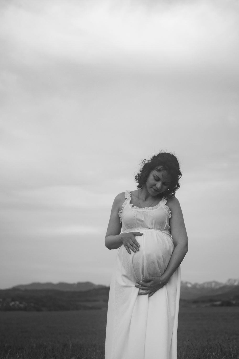 Artistic black and white maternity portrait with rolling hills in background.