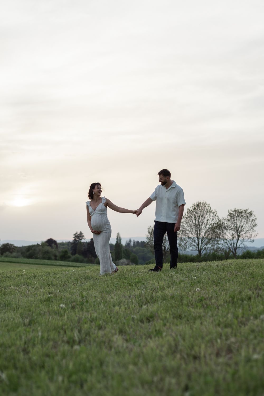 A couple walks hand in hand across a grassy hilltop during golden hour.