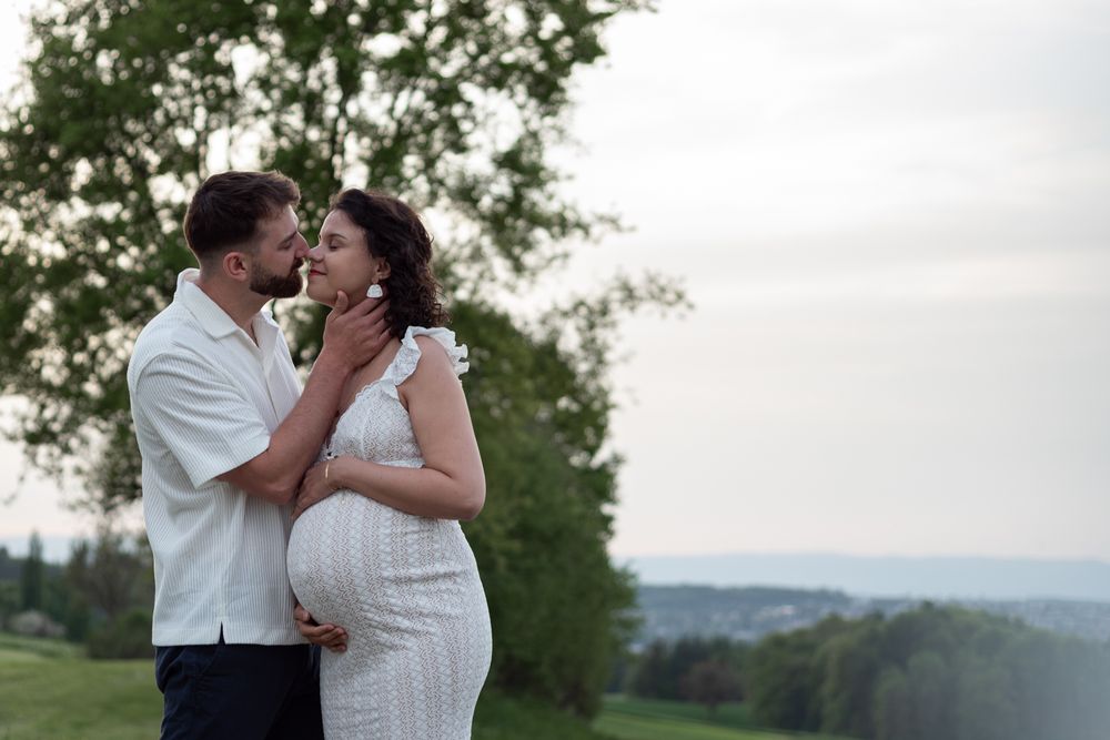 A couple shares a romantic moment in a meadow with mountains in the background.
