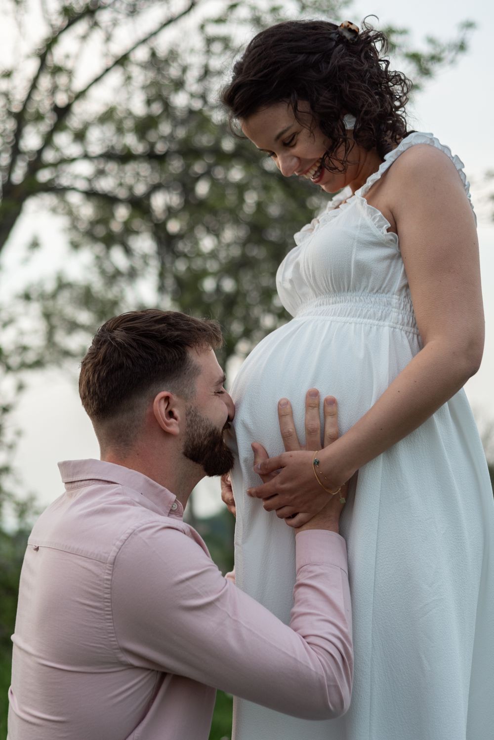 A tender maternity moment captured in soft natural lighting outdoors.