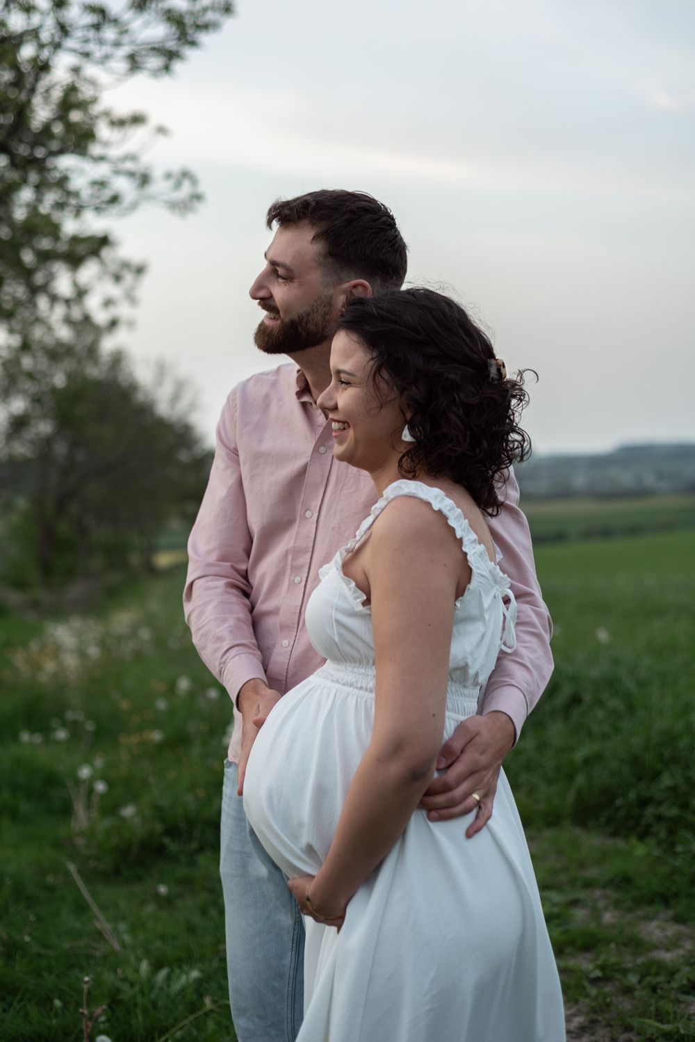 A couple shares a joyful moment during their maternity photoshoot in a green field.