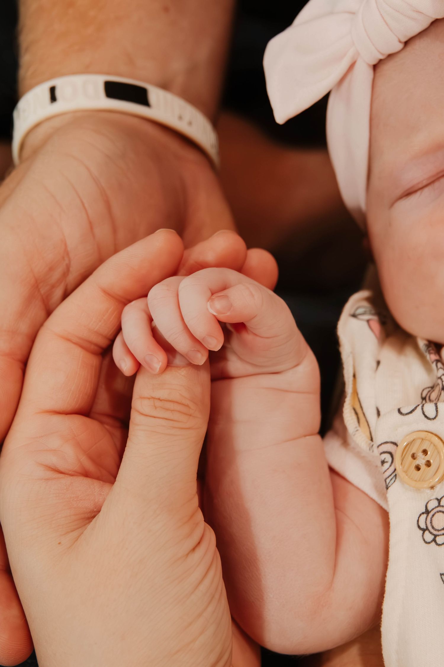 Close-up photo of tiny baby fingers grasping an adult's hand with delicate tenderness.