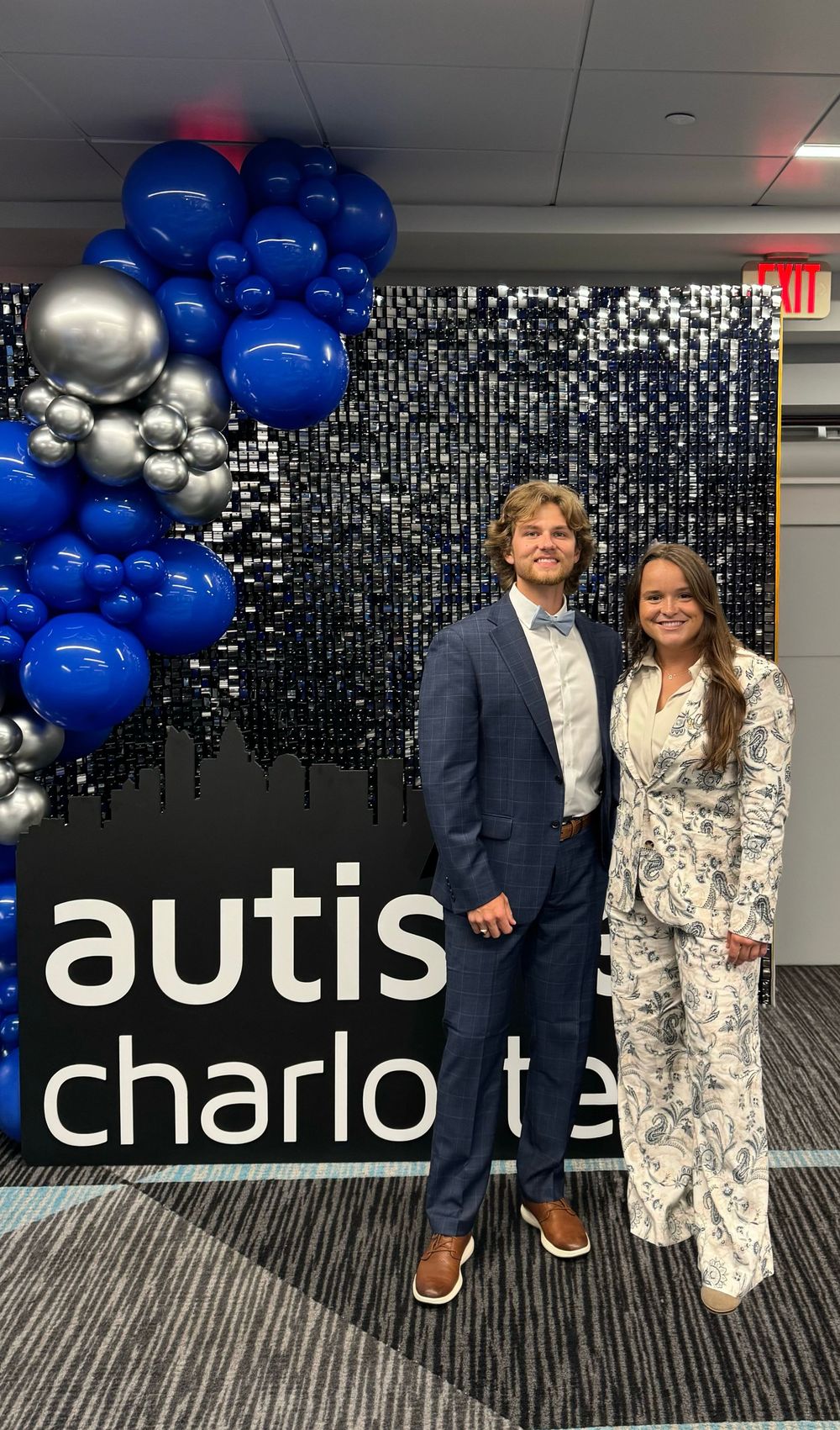 Event backdrop with black sequin wall, blue and silver balloons, and 'autis' text display for a special occasion.