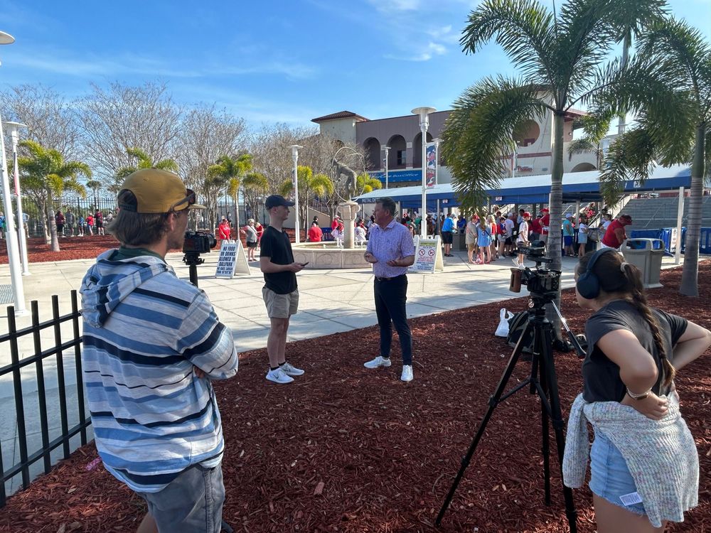 People gathered at a park on a sunny day to observe an event through telescopes near palm trees and benches.