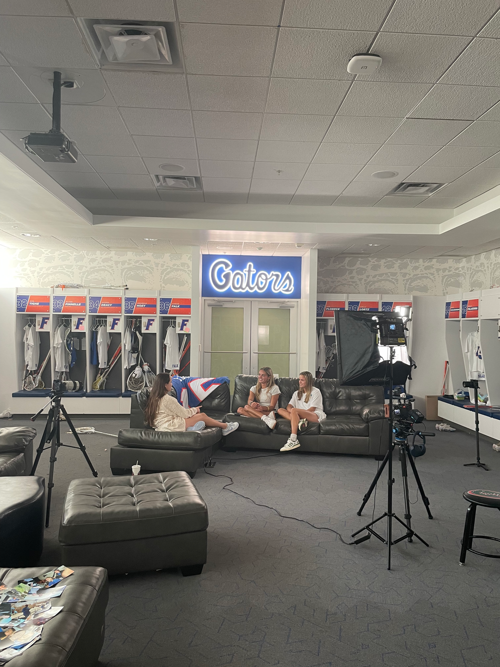 A relaxed campus lounge area with a blue Gators sign, film equipment, and people sitting on a dark gray couch.