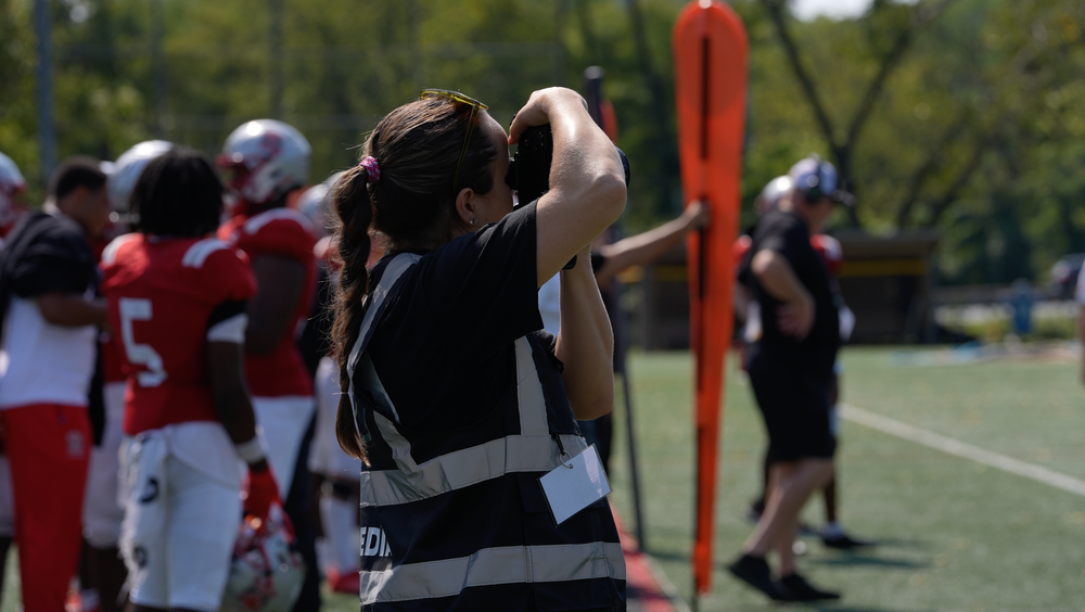 Football players practice drills on a sunny field during training camp.