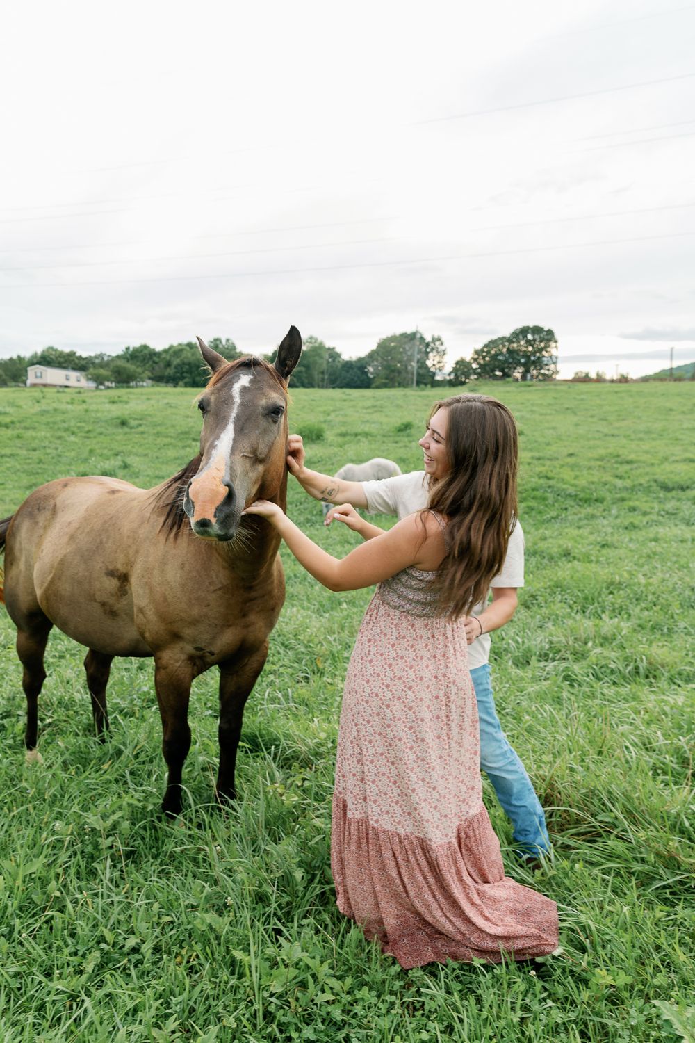 Two people pet and interact with horses in a green summer pasture.