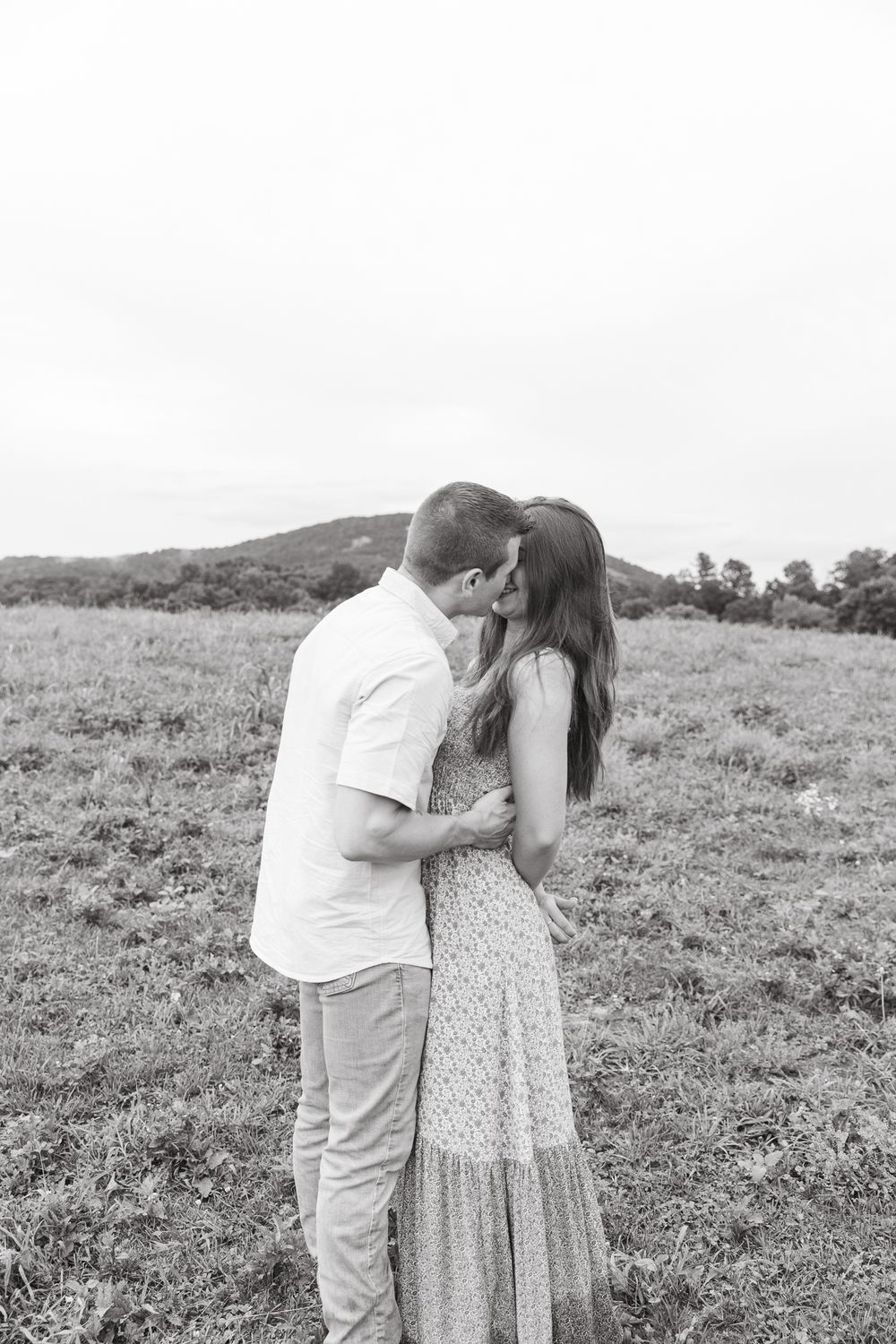 A black and white photo captures an intimate moment between a couple in a hillside field.