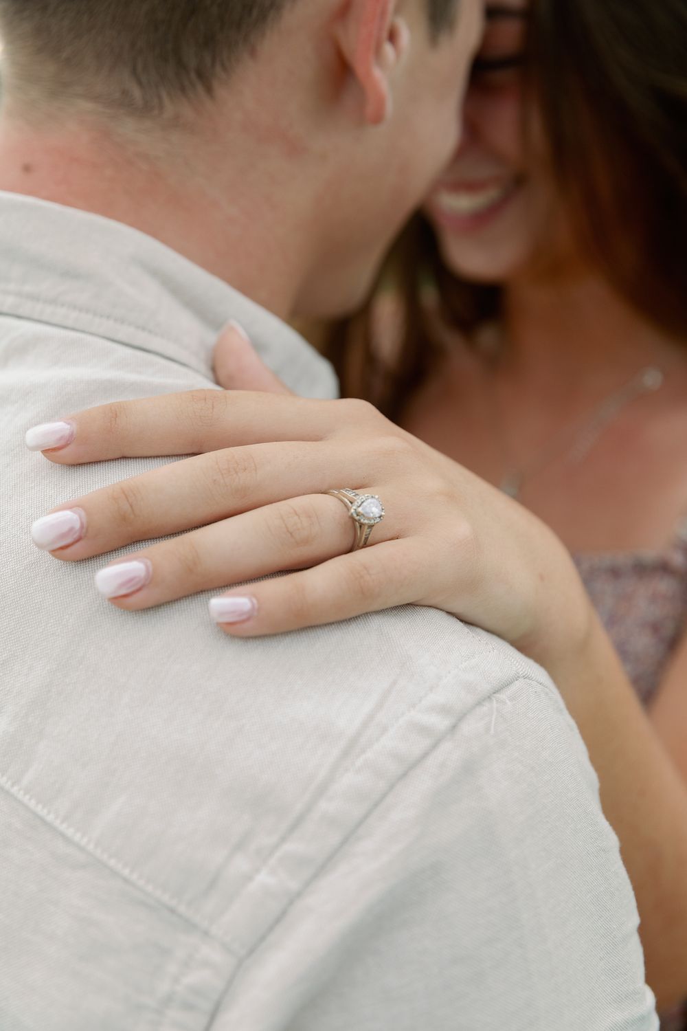 Close-up of a couple embracing with focus on hands and engagement ring.