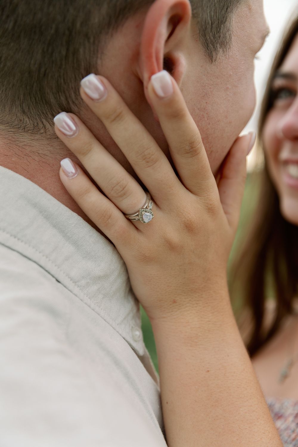 Delicate hand with engagement ring resting on shoulder detail.
