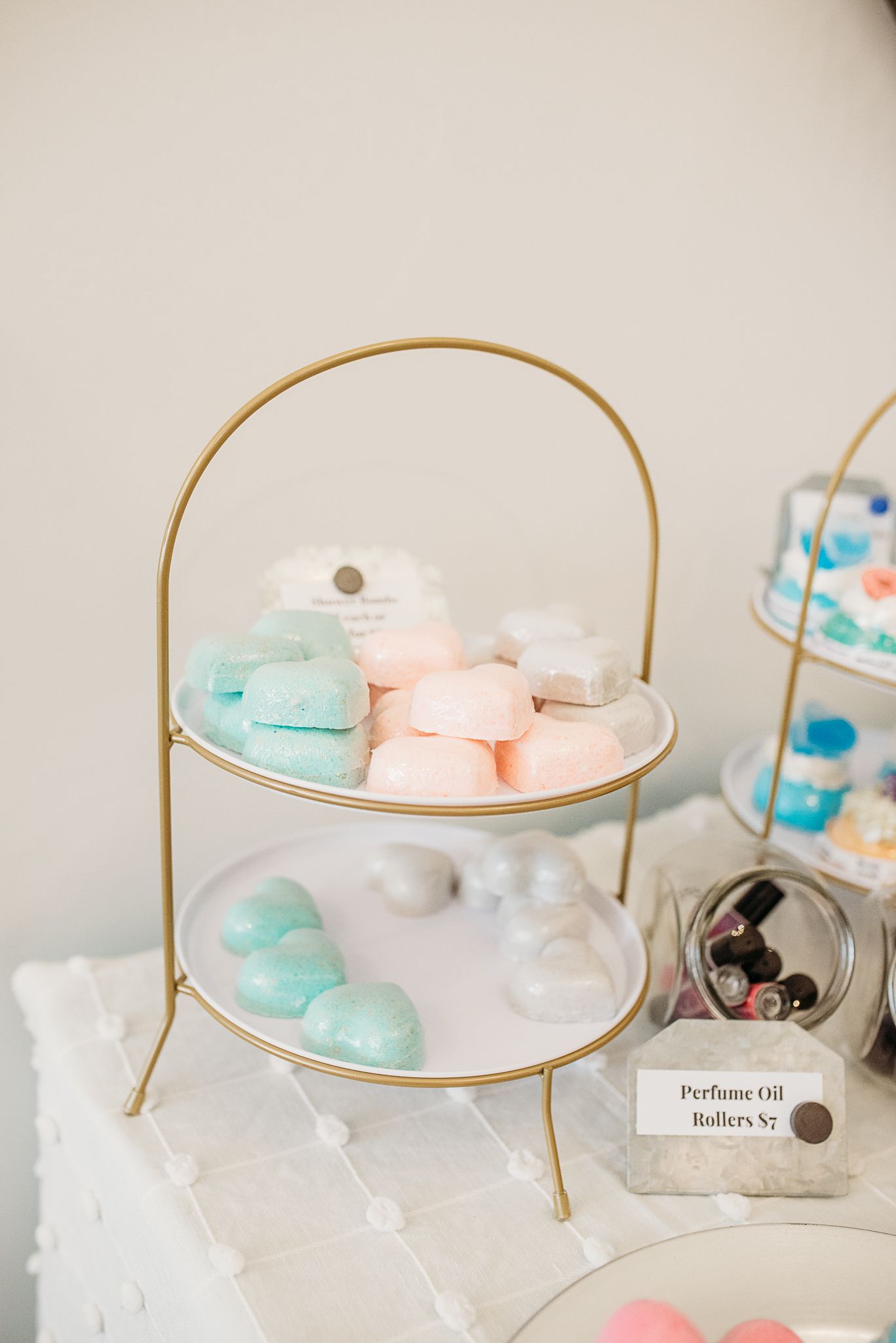 Two-tiered gold stand displaying pastel bath bombs in mint and pink colors.