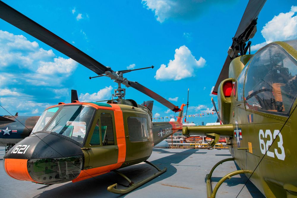 Two military helicopters on display with orange and green paint schemes.