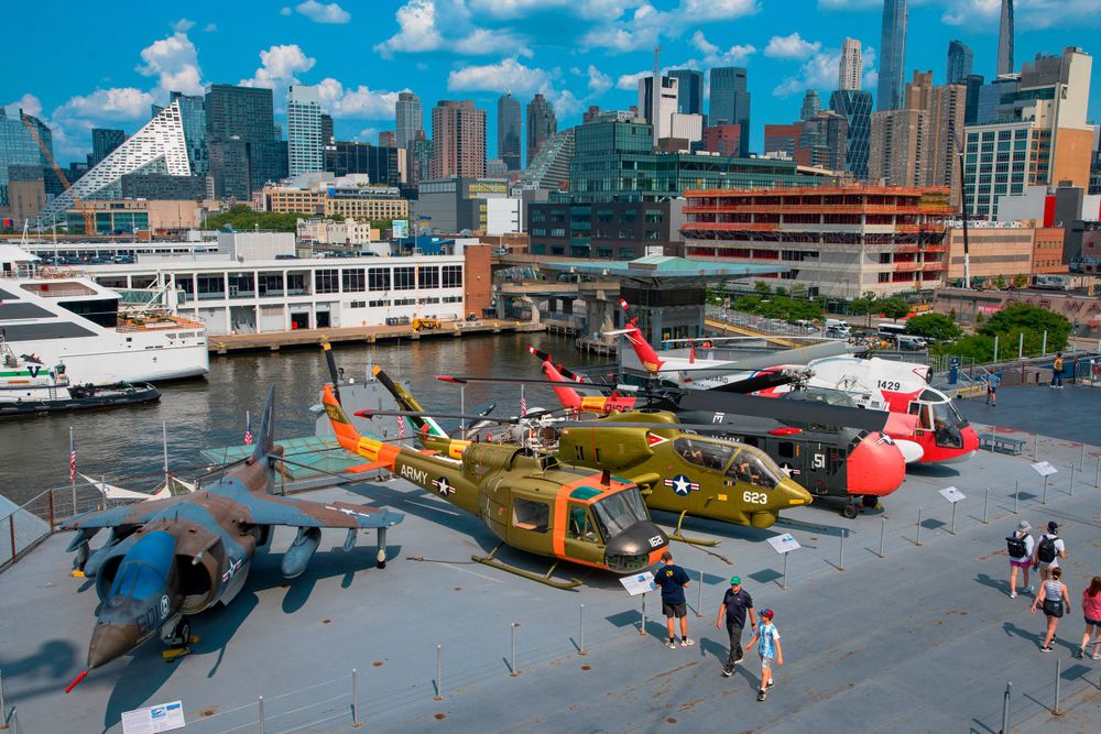 Aerial view of military aircraft display at waterfront museum with city skyline.