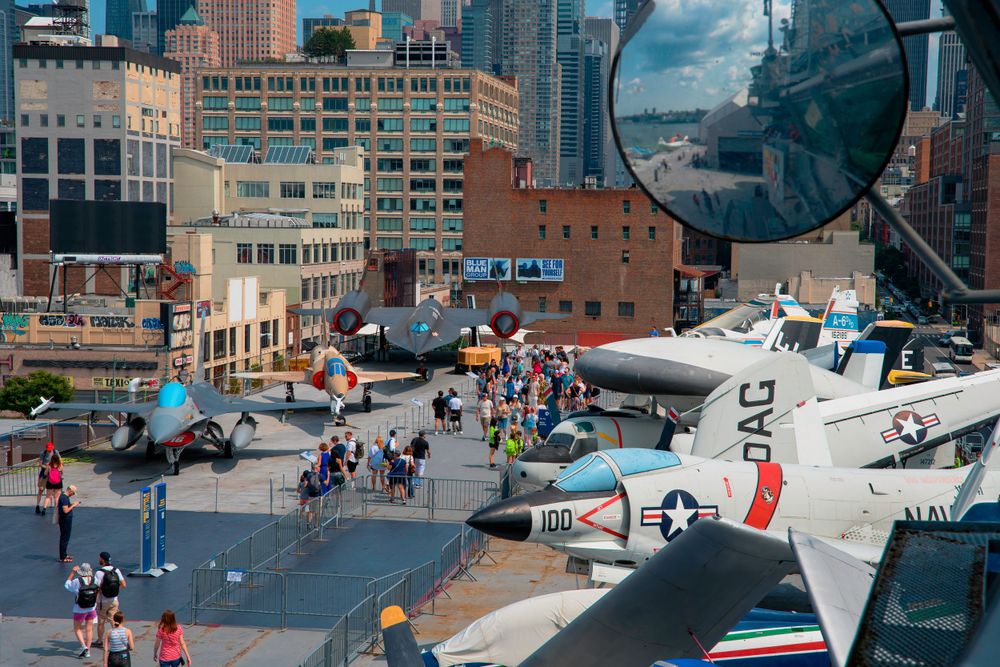 Military aircraft exhibited on museum deck with urban backdrop.