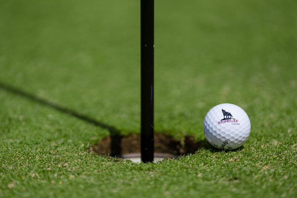 A golf ball resting next to a hole flag on manicured green grass.
