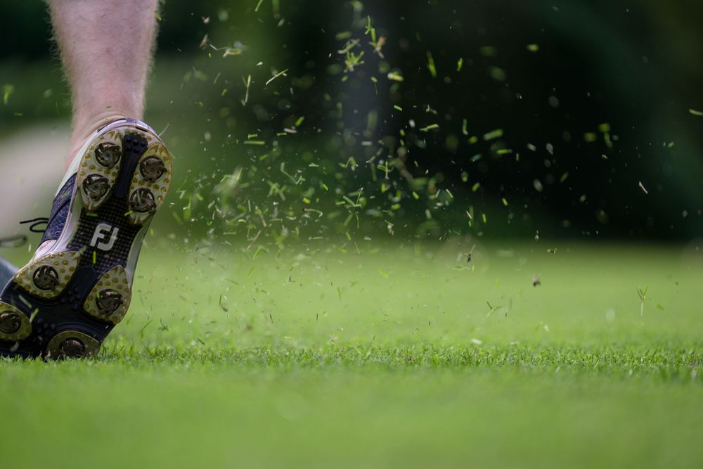 Close-up shot of grass flying from a golf club impact on a green course.