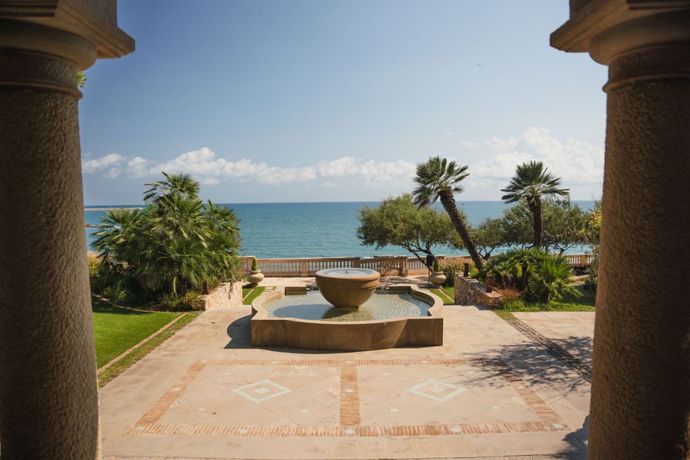 Mediterranean courtyard with stone columns framing an ocean view and decorative fountain.