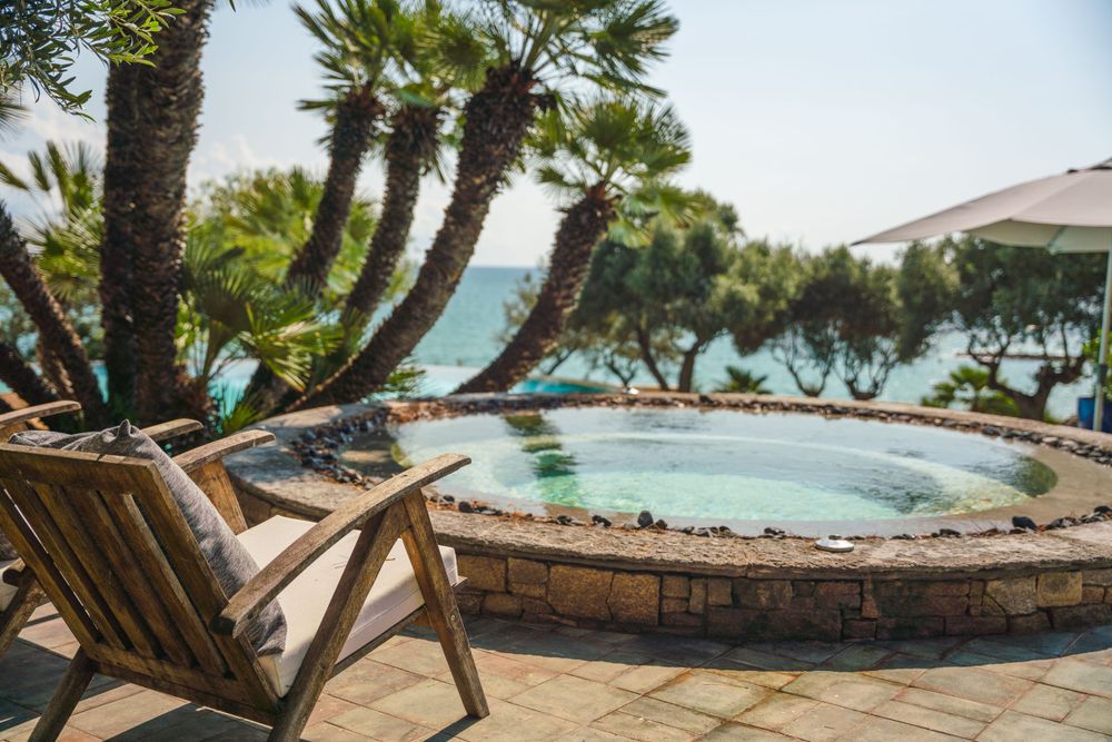 Luxury poolside lounge chairs overlooking the ocean with palm trees providing shade.