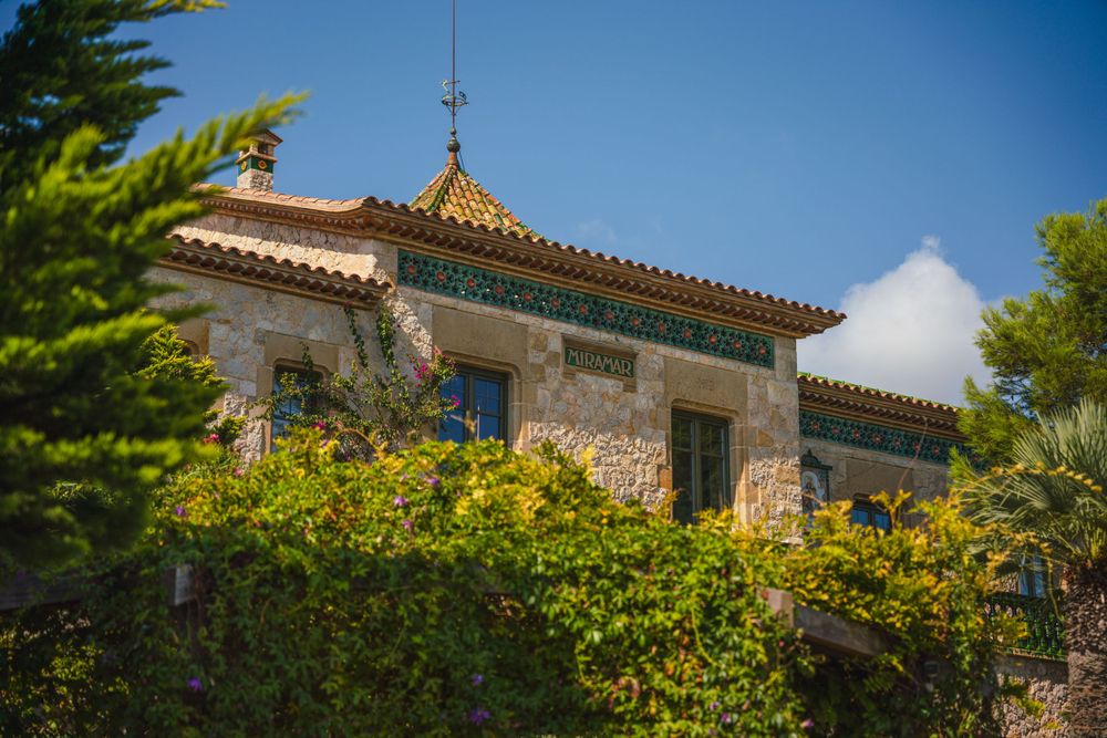 Mediterranean villa with terracotta roof and lush gardens against blue sky.