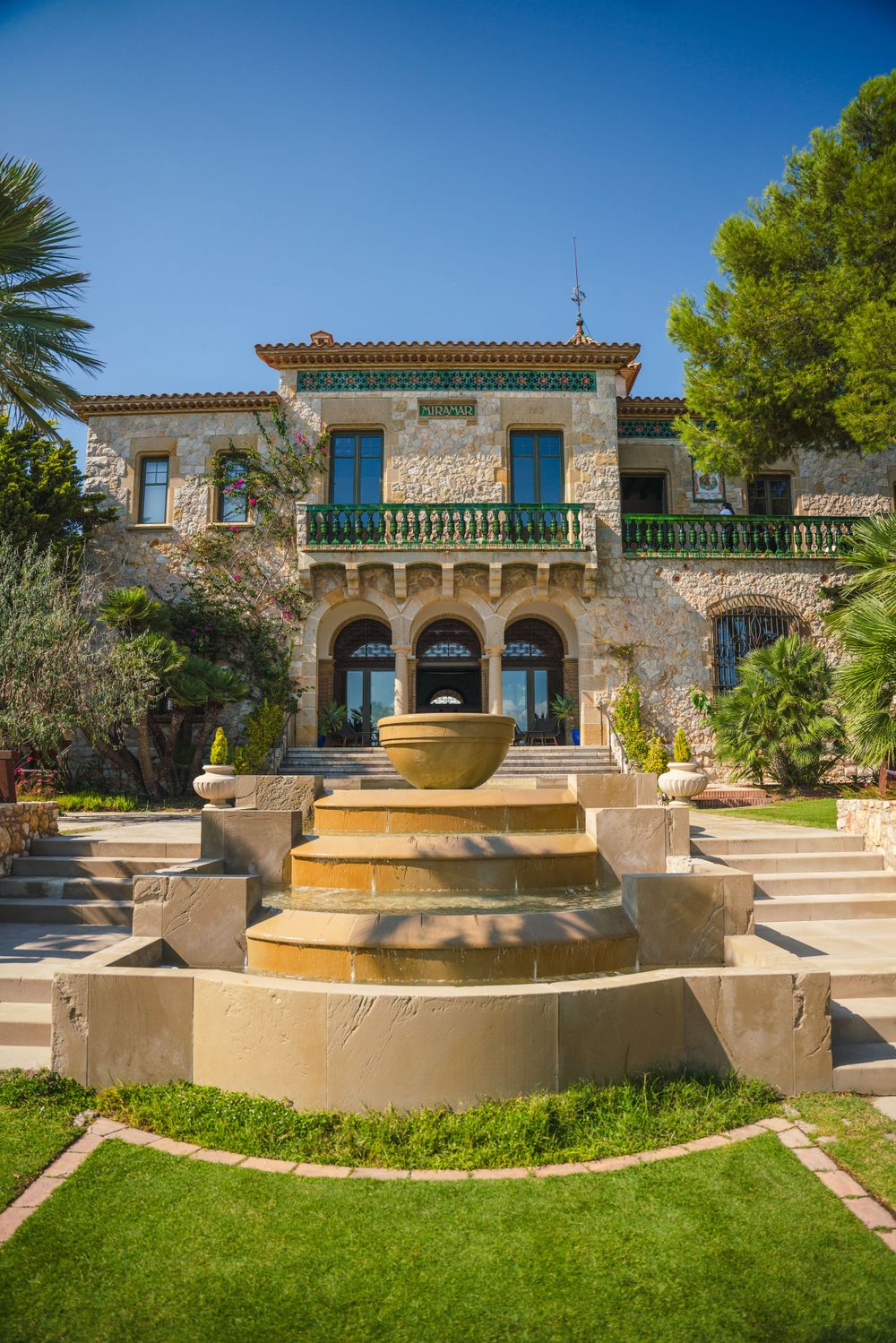 Elegant stone mansion with ornate fountain and landscaped steps leading to grand entrance.