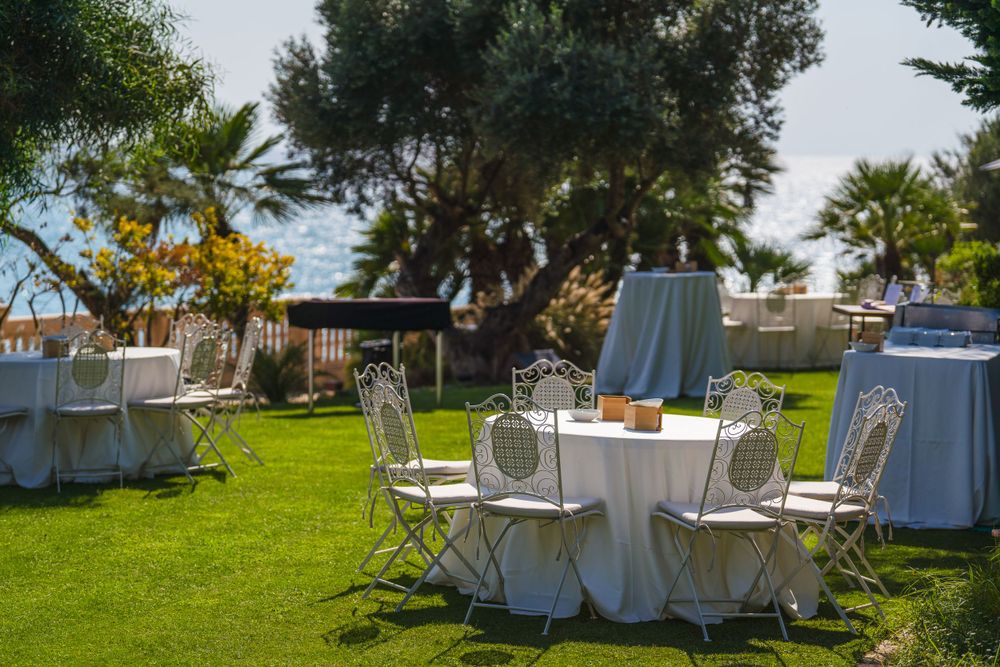 Outdoor event setup with white round tables and chairs on manicured lawn.