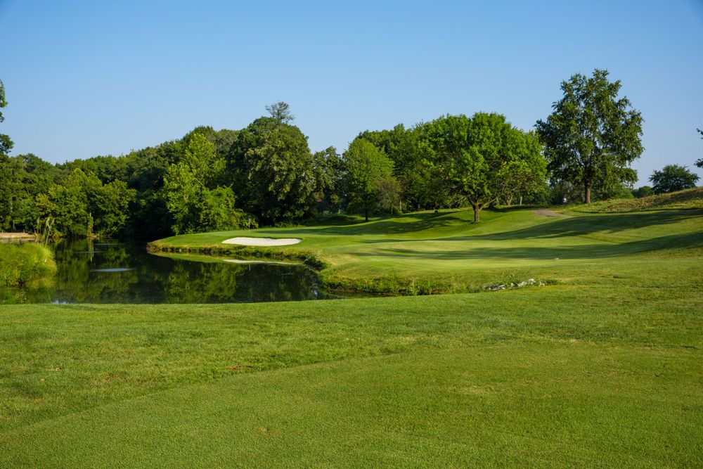 Scenic golf course with green fairway, pond, and mature trees under blue sky.