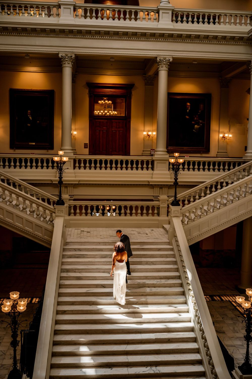 A person in white stands alone on grand marble stairs in an elegant historic building.