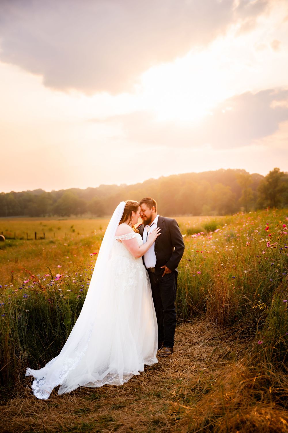 Newlyweds embrace in golden sunset light among wildflowers.