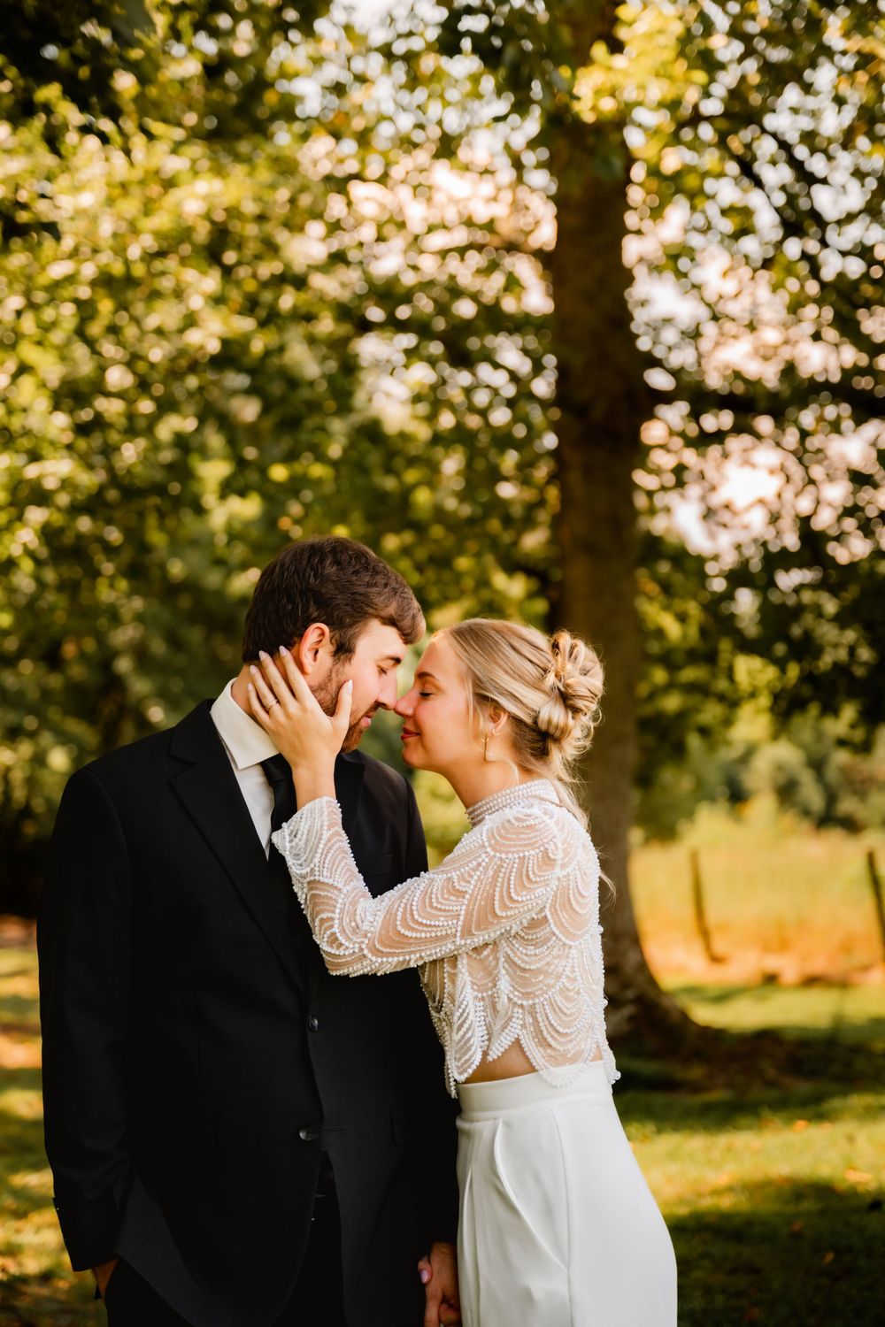 Romantic wedding couple sharing a tender kiss in a sunlit garden with golden bokeh through the trees.