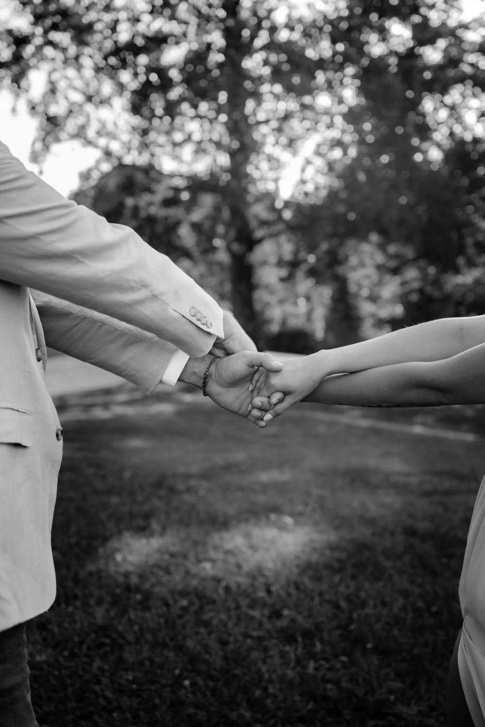 Black and white photo of a couple holding hands outdoors, with blurred trees in the background.