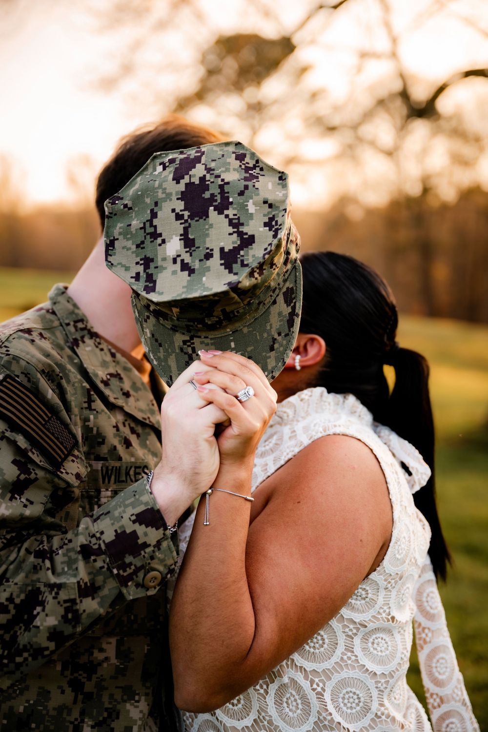 A tender moment between a couple in military uniform and wedding dress at sunset during an outdoor ceremony.