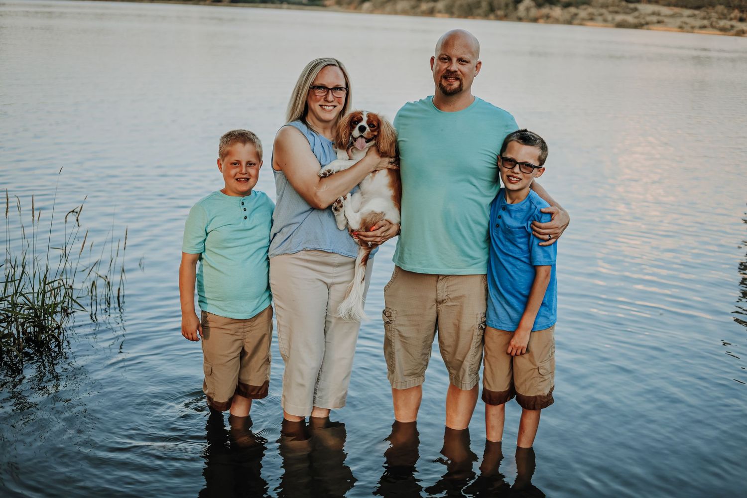 Family portrait by the water during sunset with everyone wearing coordinated casual outfits.