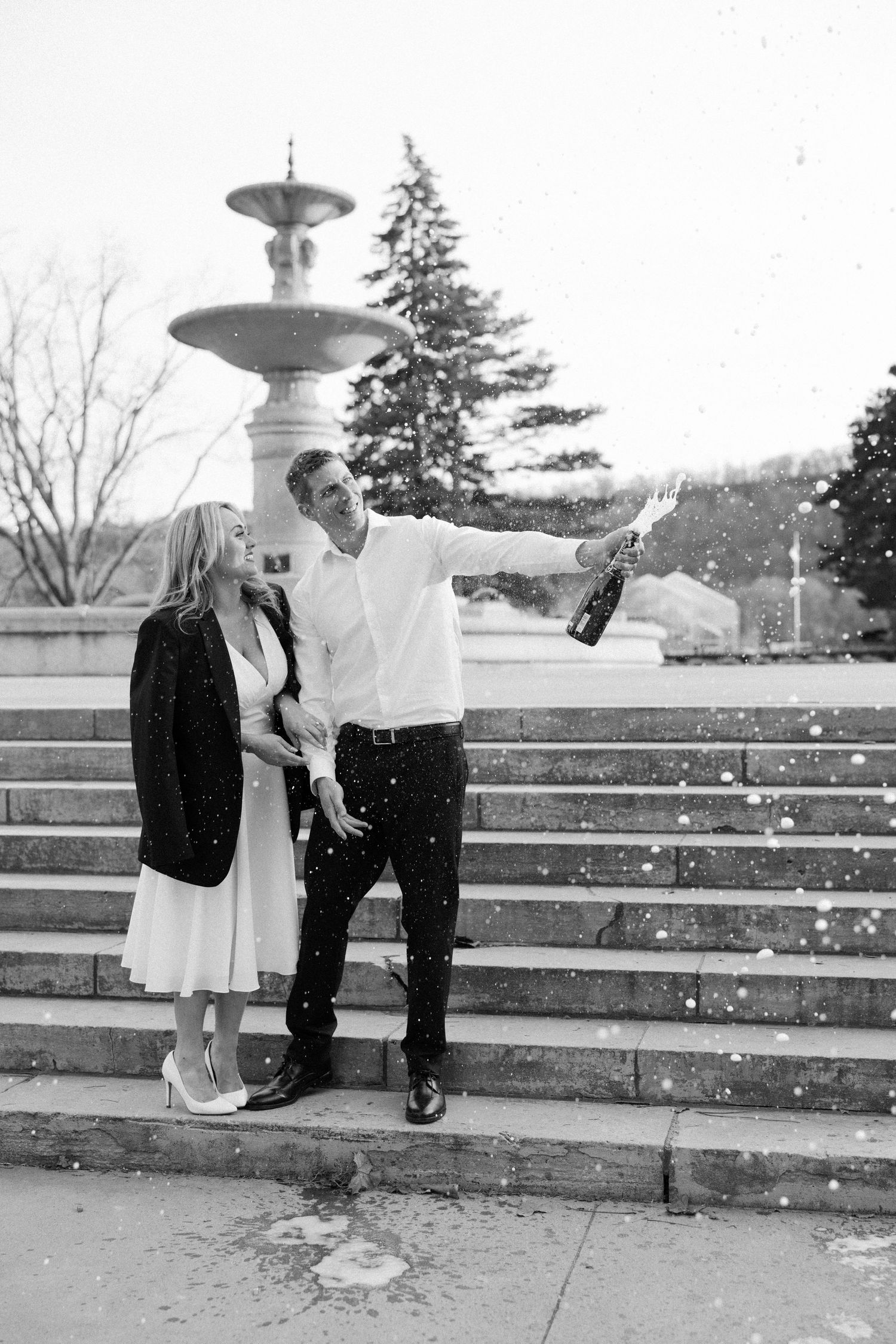 Candid black-and-white wedding portrait of newlyweds celebrating with a champagne pop in Hamilton, Ontario