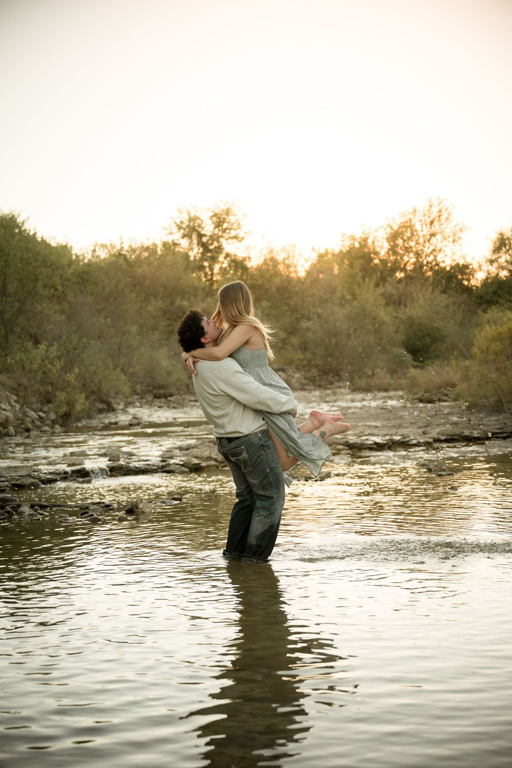 Engagement photography session in Dallas–Fort Worth with couple embracing at golden hour in creek