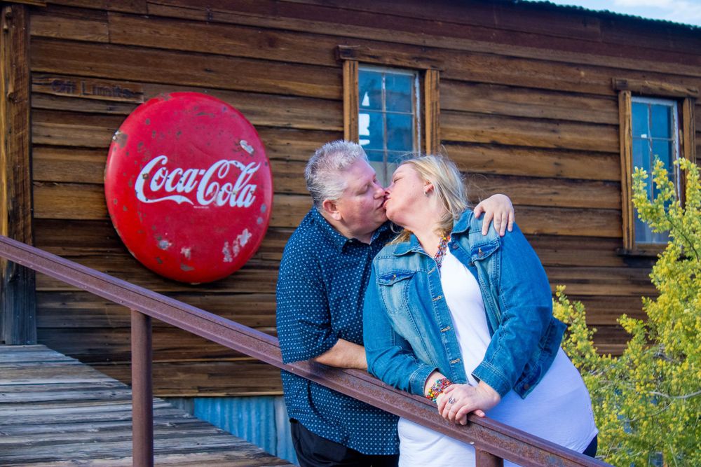 Couple kissing on wooden porch steps beside vintage Coca-Cola sign on rustic log cabin wall.