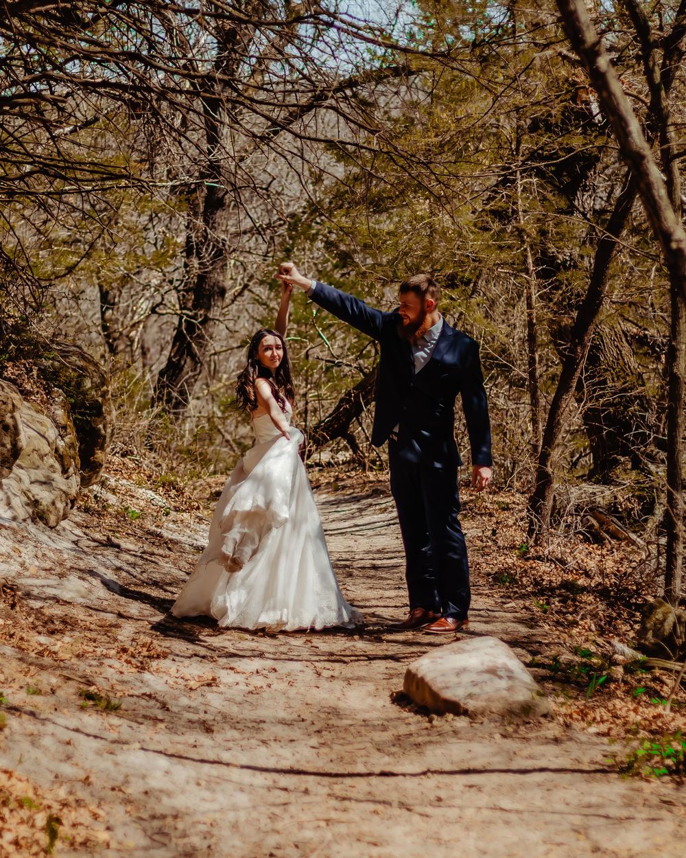 A couple shares a playful moment on a wooded trail during their wedding photoshoot.