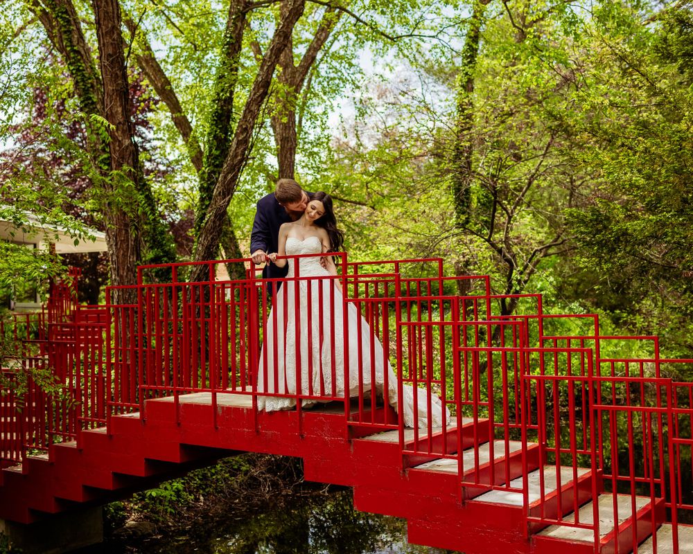 Newlyweds share an intimate moment on vibrant red stairs in a garden setting.