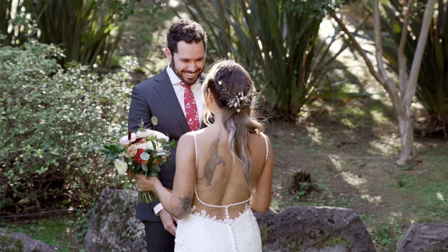 A bride and groom share a special moment together in a lush garden setting with tropical plants and flowers.