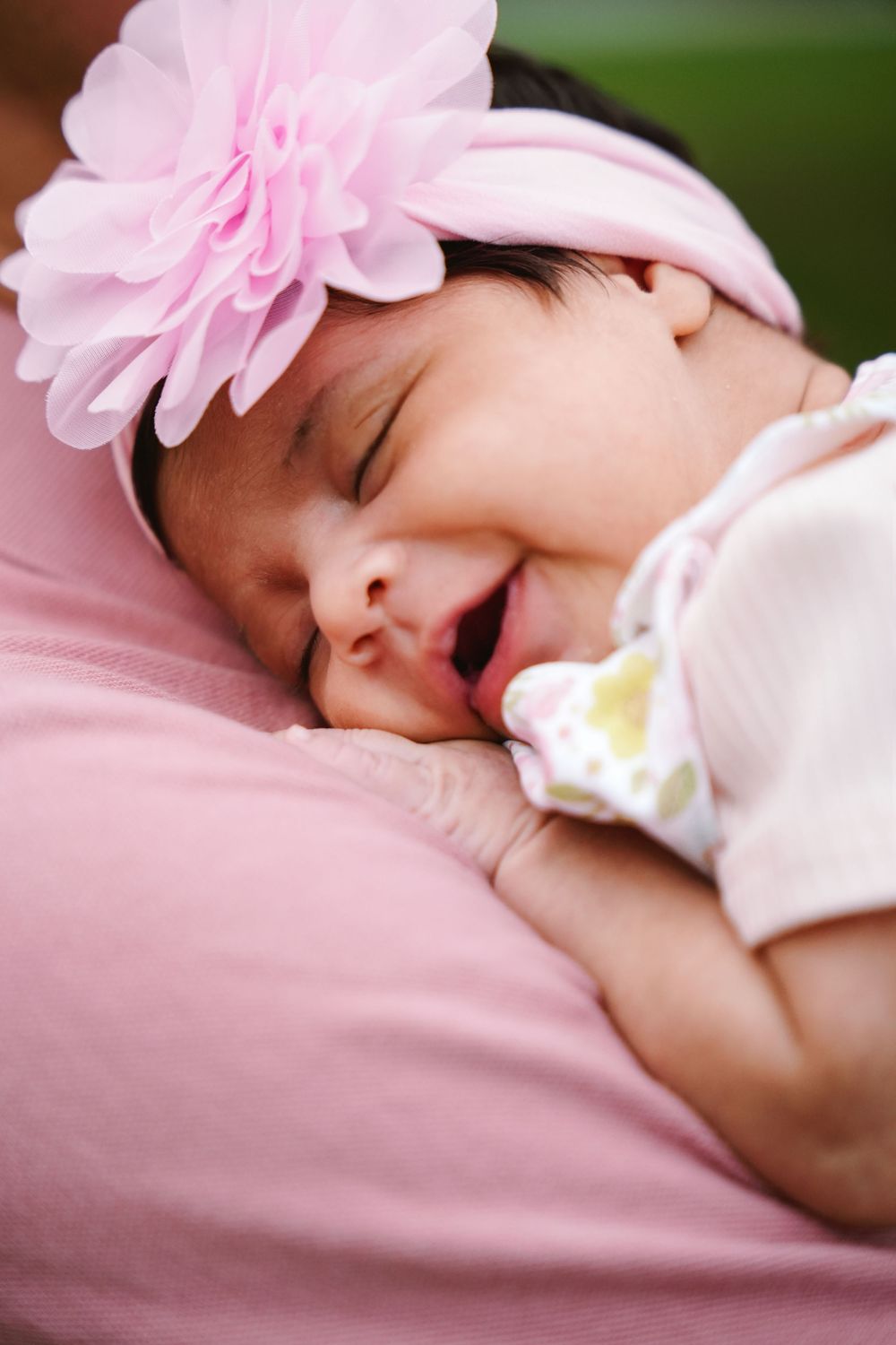 Sleeping newborn baby girl wearing a pink floral headband, resting peacefully on a soft pink surface. Toronto GTA