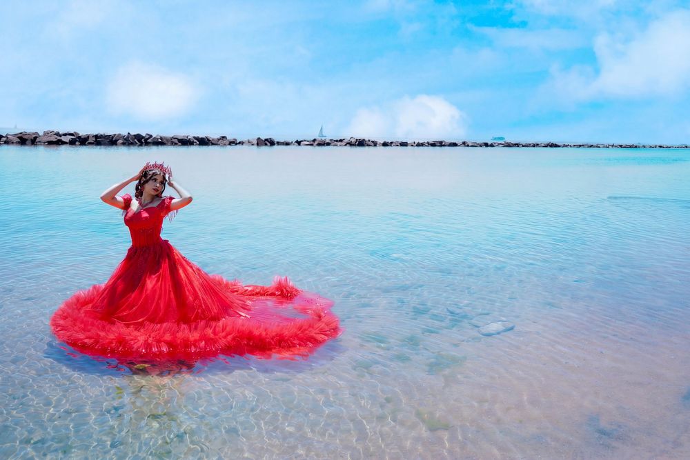 Woman in red ballgown standing in shallow turquoise ocean waters under a bright blue sky. Toronto GTA