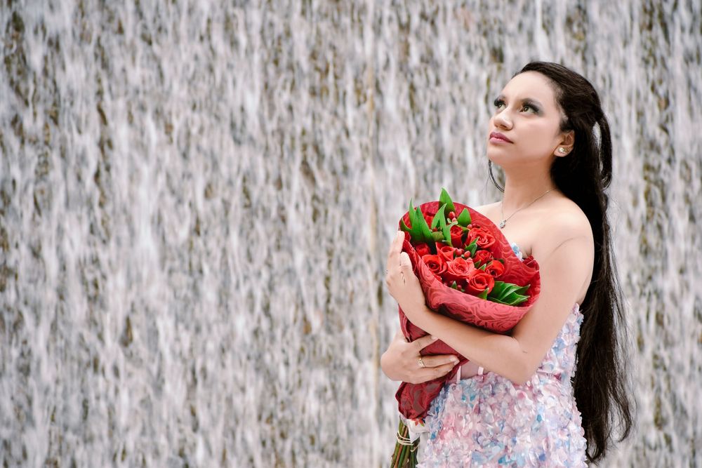 Young woman in floral dress holding red roses bouquet standing before a cascading waterfall backdrop. Toronto GTA
