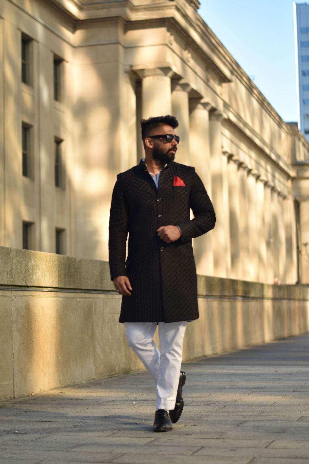 Stylish man in black quilted coat and white pants walks confidently along a grand building. Toronto GTA