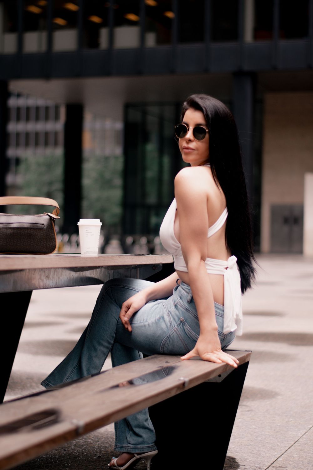 Woman in white top and jeans sits at outdoor table with coffee cup and sunglasses on. Toronto GTA